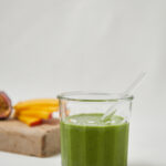 glas with green smoothie and straw fresh mango in the back