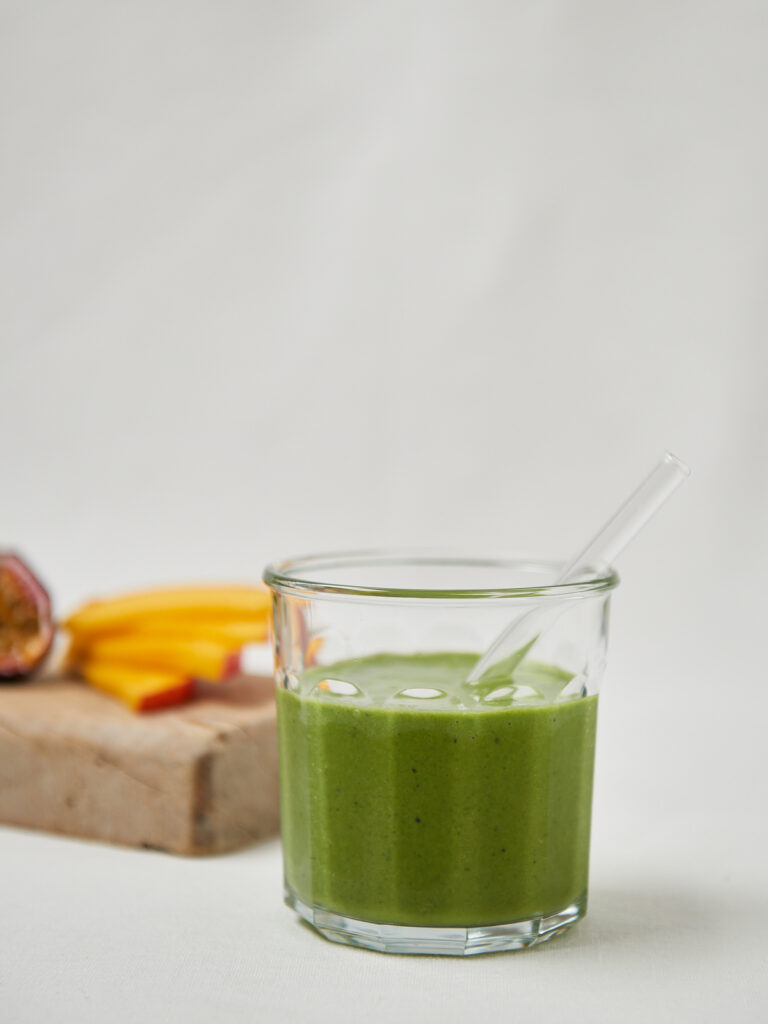 glas with green smoothie and straw fresh mango in the back