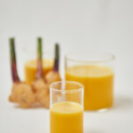 2 glasses with ginger shots and a ginger root