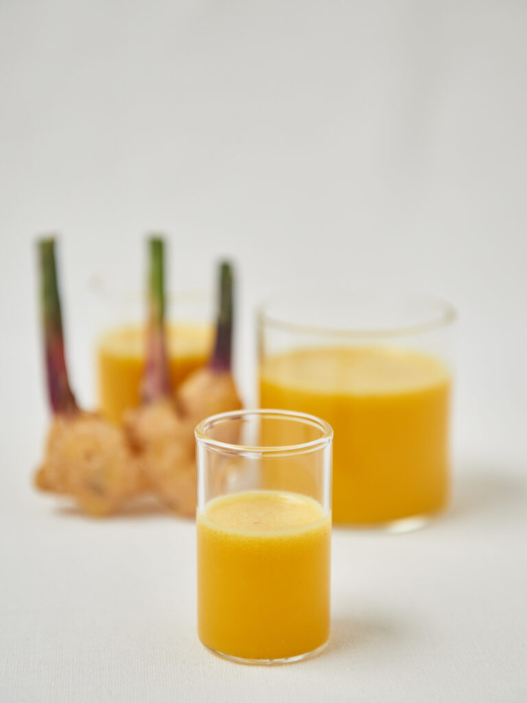 2 glasses with ginger shots and a ginger root