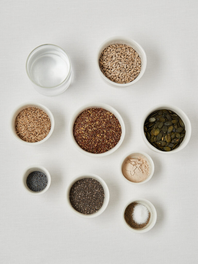 Flatlay of fiber cracker ingredients including chia seeds, flaxseeds, pumpkin seeds and spices in small bowls.