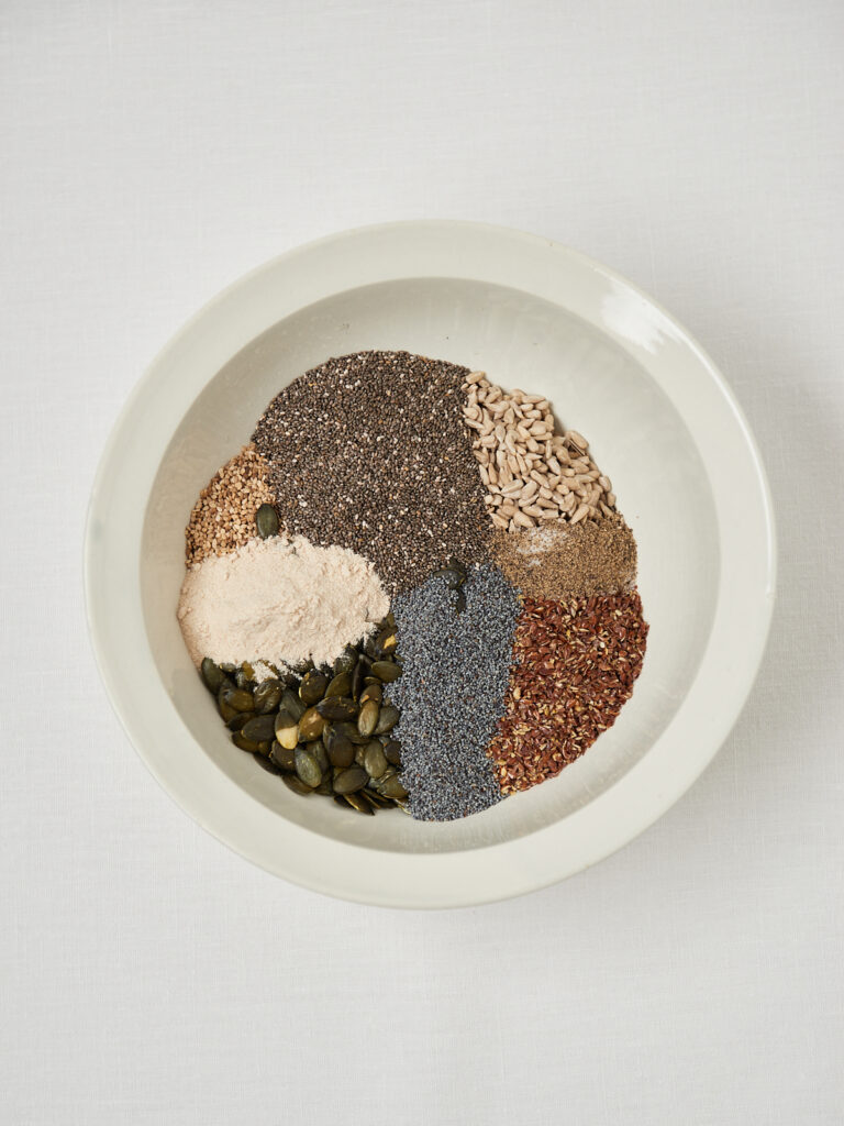 Top view of chia seeds, flaxseeds, sunflower seeds, pumpkin seeds and fiber powder arranged neatly in a white bowl.