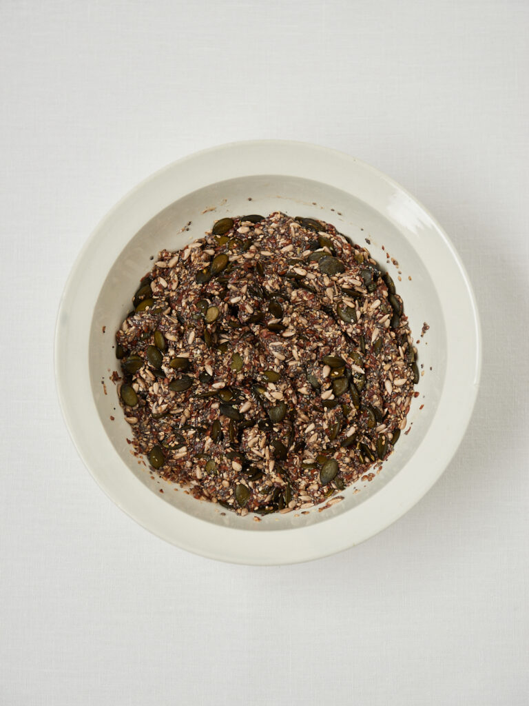 Seed mixture for homemade fiber crackers after adding water and mixing, shown in a white bowl.