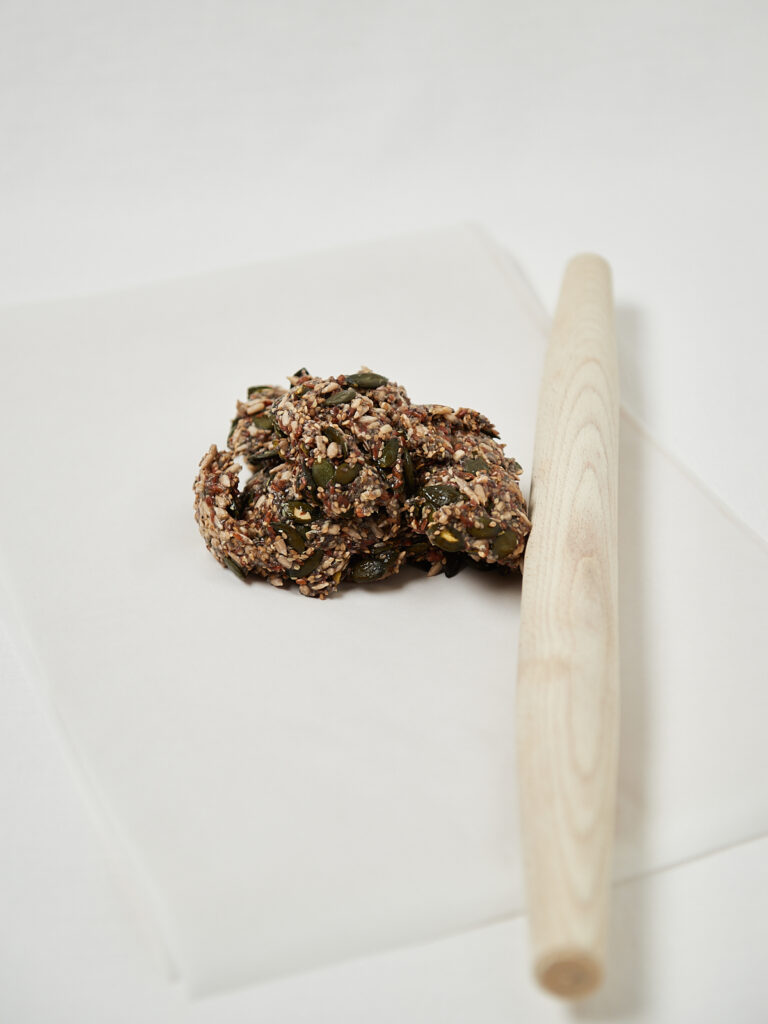 Small mound of mixed seed cracker dough on parchment paper before spreading.