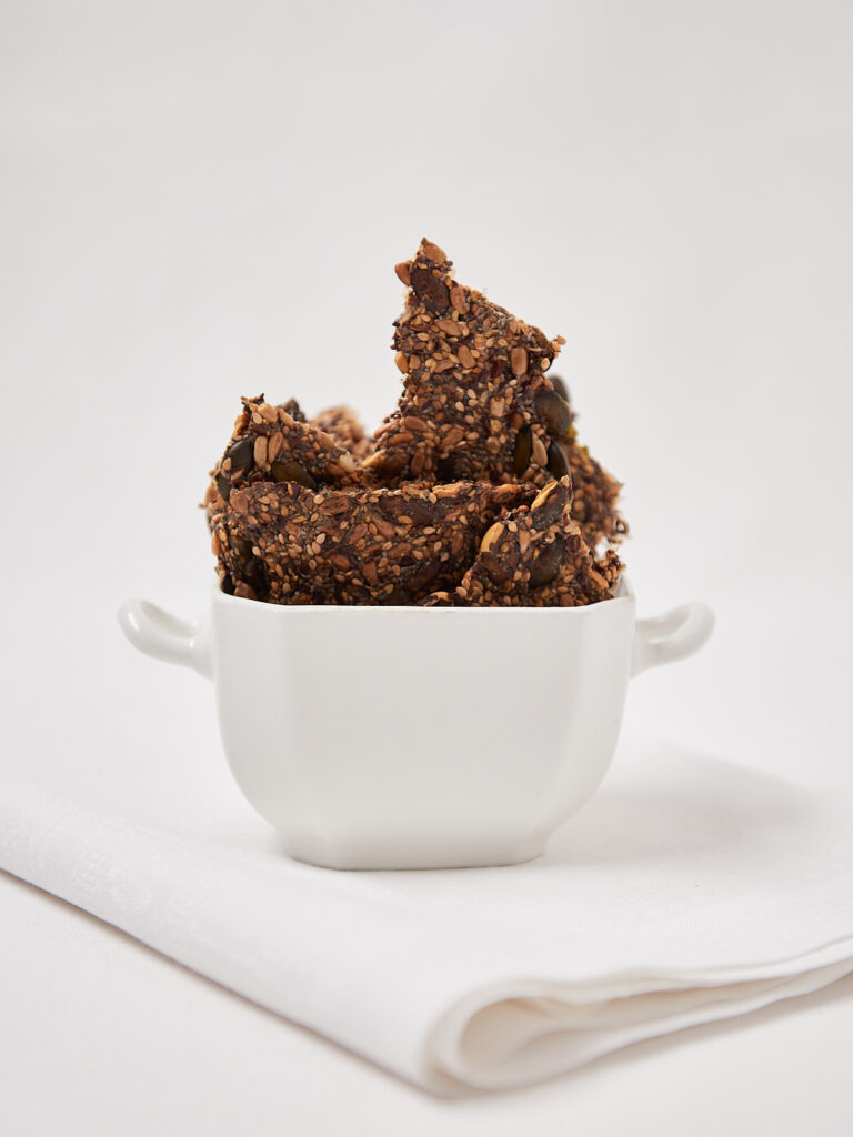 Homemade crunchy seed and nut crackers piled in a small white ceramic bowl.