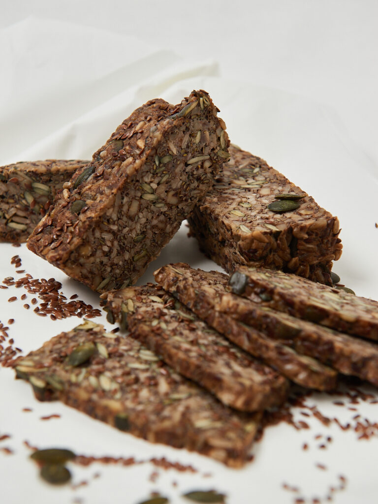 Mehrkorn-Life-Changing-Bread in Scheiben geschnitten, mit sichtbaren Nüssen, Kernen und Samen auf hellem Untergrund.