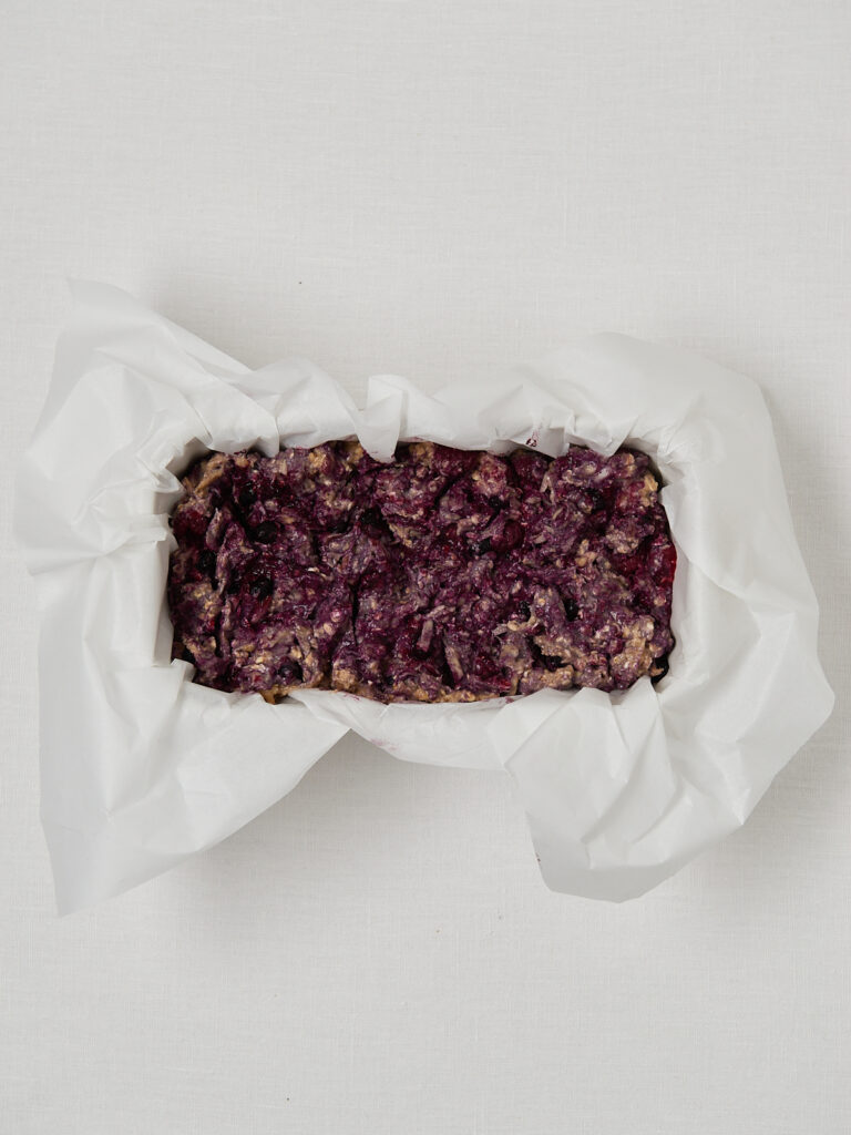 Purple-swirled berry banana bread batter placed into a loaf pan lined with parchment paper before baking.