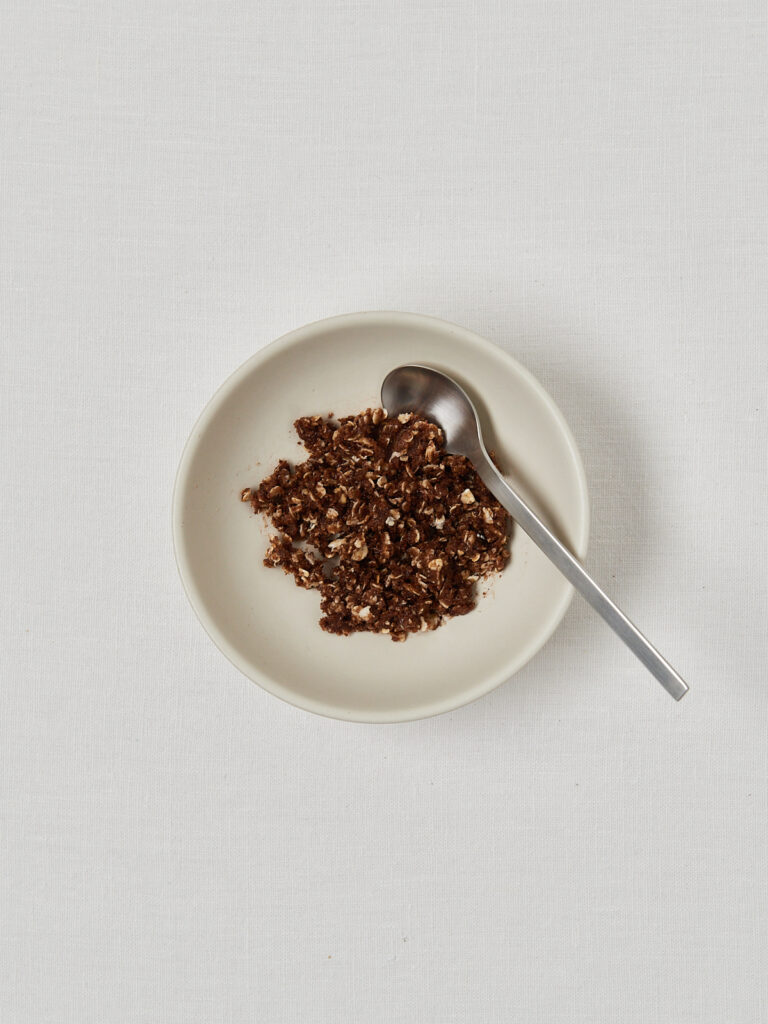 Prepared crumble topping of oats, sugar, cinnamon and oil stirred together in a white bowl.