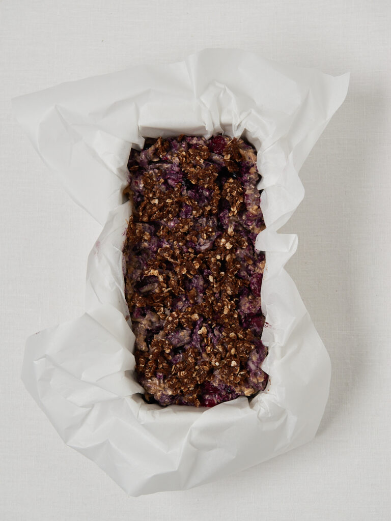 Unbaked berry banana bread with cinnamon oat crumble topping, placed in a loaf pan lined with parchment paper.
