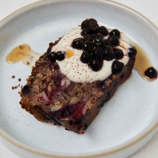 Slice of moist berry banana bread served with creamy yogurt, blueberries and a drizzle of syrup.