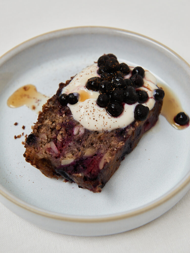 Slice of moist berry banana bread served with creamy yogurt, blueberries and a drizzle of syrup.
