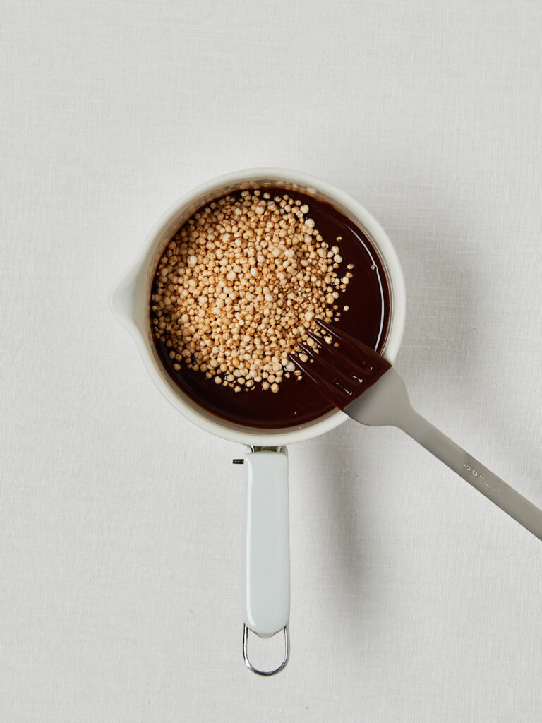 Messbecher mit geschmolzener Schokolade und Haselnussmus, in die gepuffter Quinoa eingerührt wird.