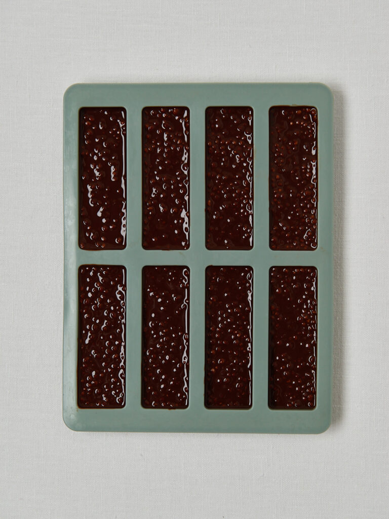 Schokoladen-Haselnuss-Quinoa-Masse in einer grünen Silikonform zum Festwerden vorbereitet.