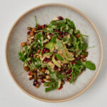 white bowl with veggies and arugola salat and tahini dressing photographed from above