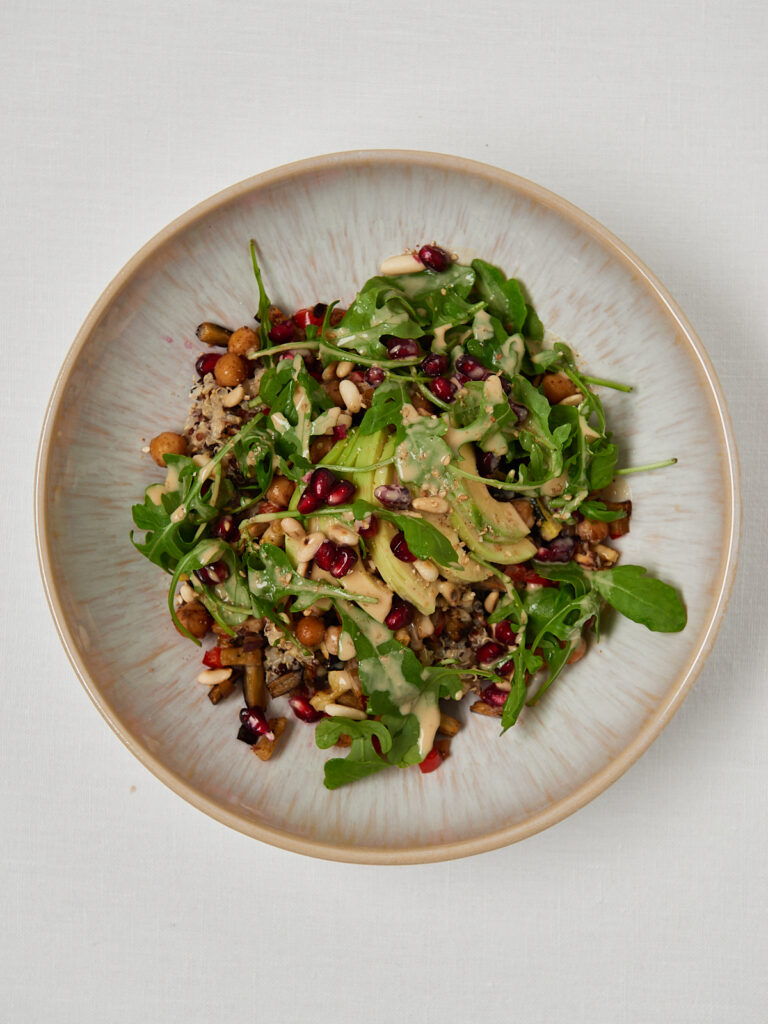 white bowl with veggies and arugola salat and tahini dressing photographed from above