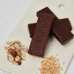 Fertige Schoko-Haselnuss-Riegel mit gepufftem Quinoa, angerichtet auf einem weißen Brett mit Haselnussstücken und Quinoa.