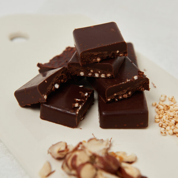 Healthy hazelnut chocolate bites with crunchy puffed grains, stacked on a white board with chopped hazelnuts.