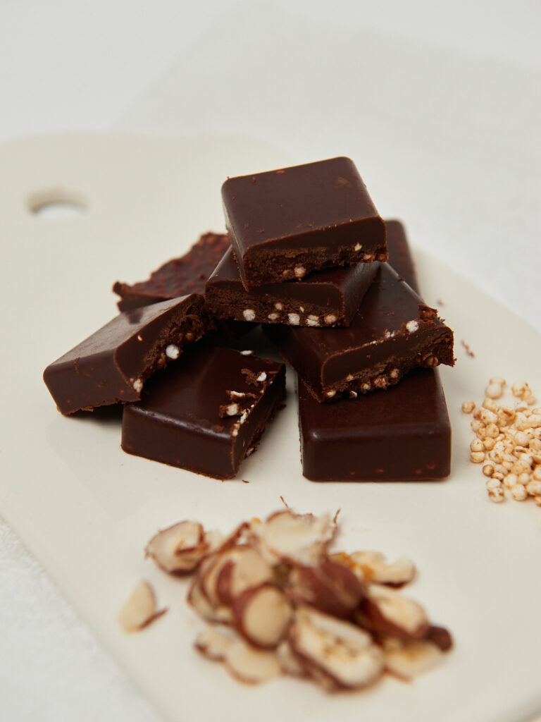 Healthy hazelnut chocolate bites with crunchy puffed grains, stacked on a white board with chopped hazelnuts.