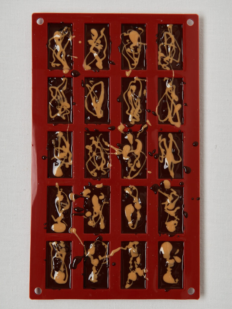 Rote Silikonform gef&uuml;llt mit Schoko-Erdnuss-Fudge, marmoriert mit Erdnussmus.