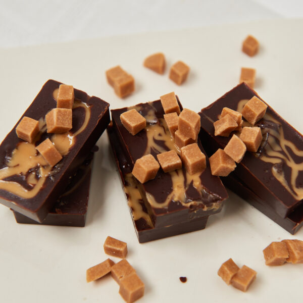 Schokoladenriegel mit kleinen Haselnuss-Stückchen, gestapelt auf einem weißen Untergrund.