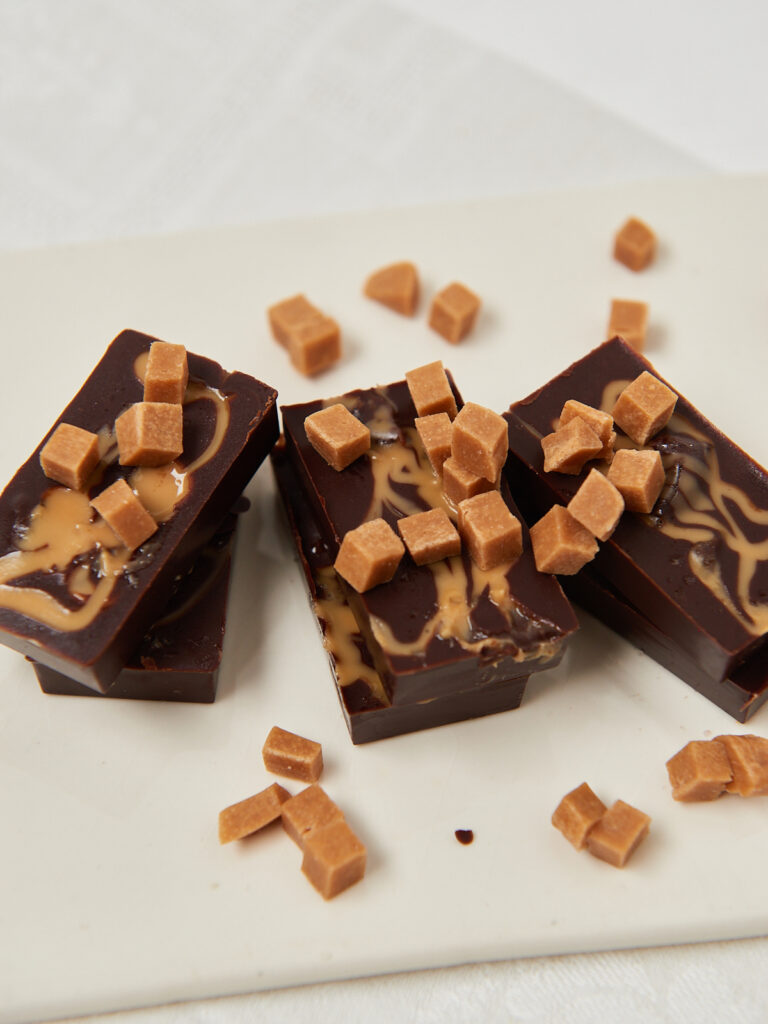 Schokoladenriegel mit kleinen Haselnuss-St&uuml;ckchen, gestapelt auf einem wei&szlig;en Untergrund.