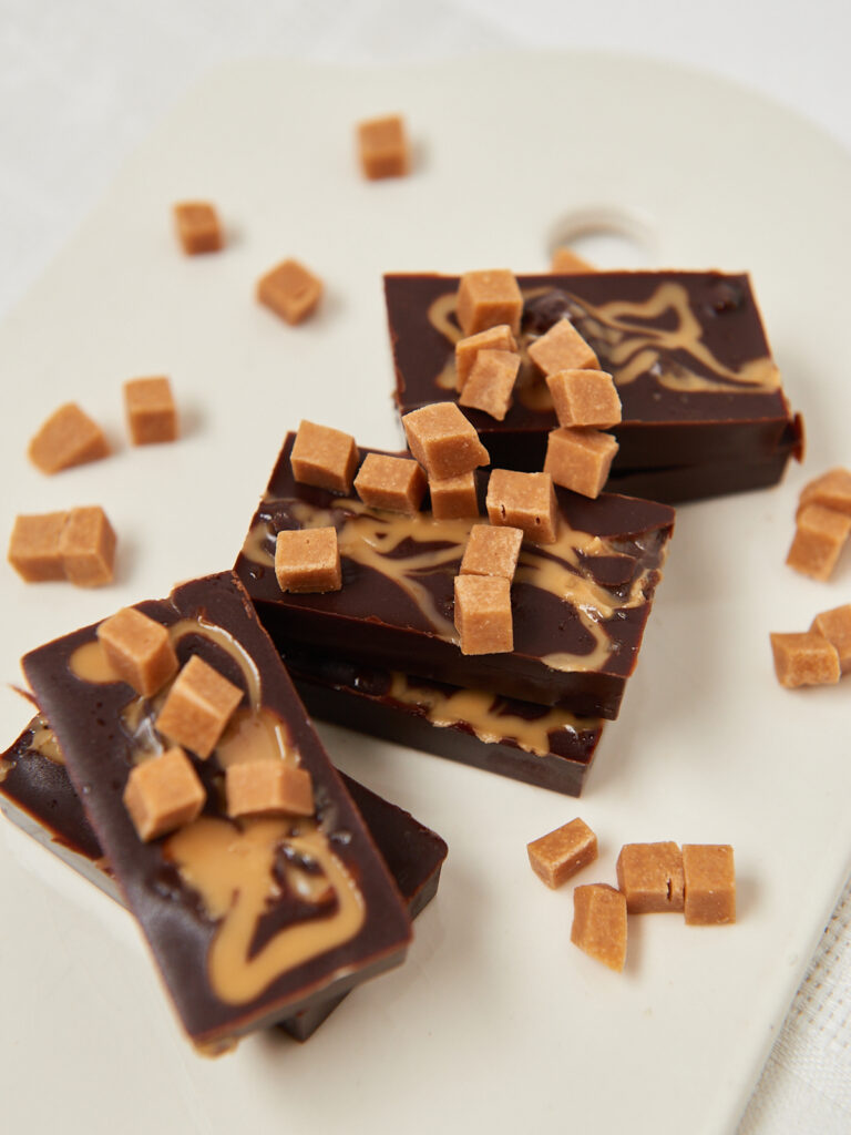 Gestapelte Schoko-Fudge-St&uuml;cke mit Erdnuss-Swirl und kleinen Dattelw&uuml;rfeln auf einem hellen Untergrund.