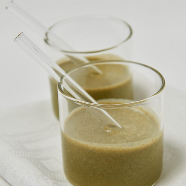 Zwei Gläser mit grünem Smoothie und Glasstrohhalmen auf einem weißen Tuch.