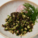 Quinoa and black lentil salad topped with fresh herbs served in a white ceramic bowl.