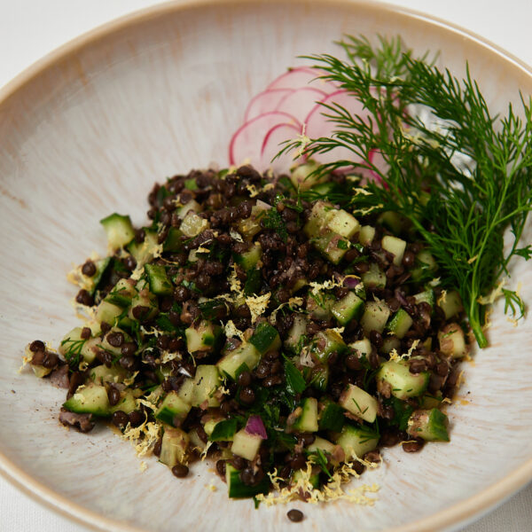 Quinoa and black lentil salad topped with fresh herbs served in a white ceramic bowl.