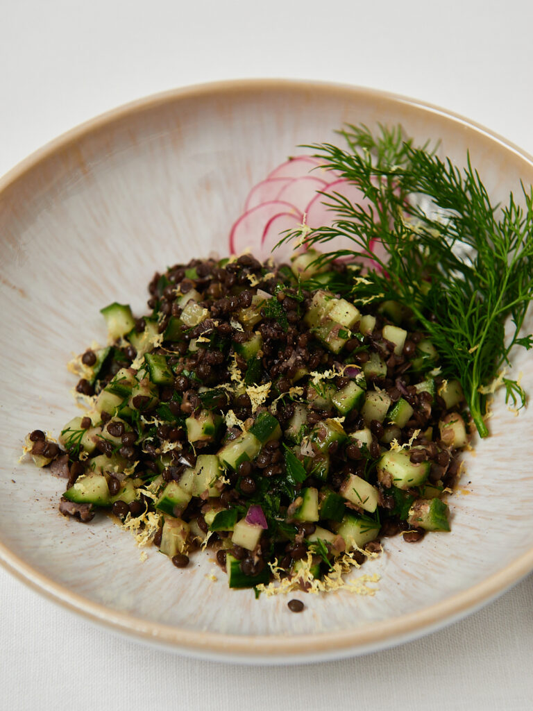Quinoa and black lentil salad topped with fresh herbs served in a white ceramic bowl.
