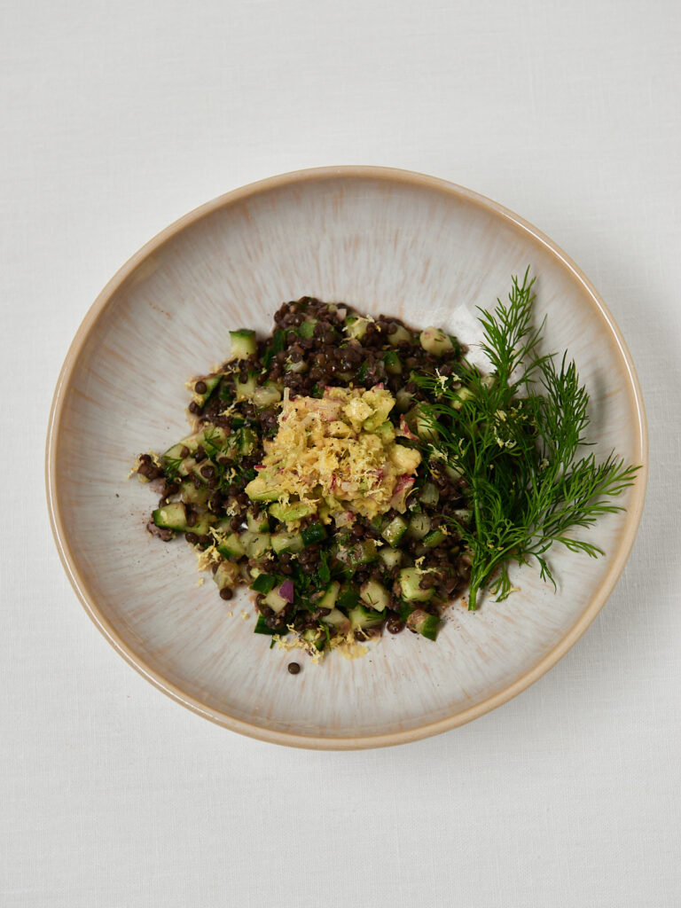 Quinoa and black lentil salad topped with fresh herbs served in a white ceramic bowl.