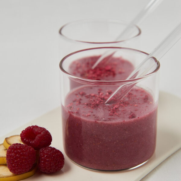 two glasses with delicious pink smoothie with glass straws and raspberries