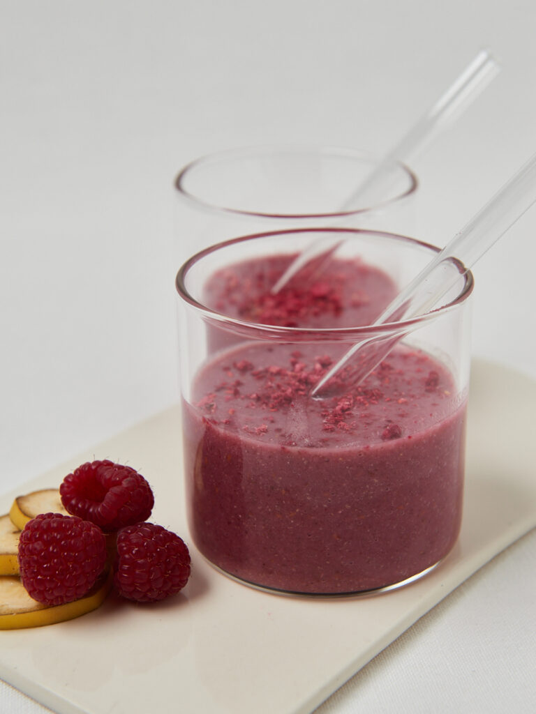 two glasses with delicious pink smoothie with glass straws and raspberries