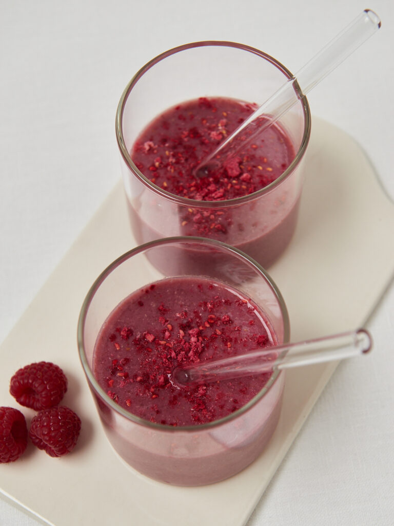 two glasses with pink smoothie and raspberries decorated