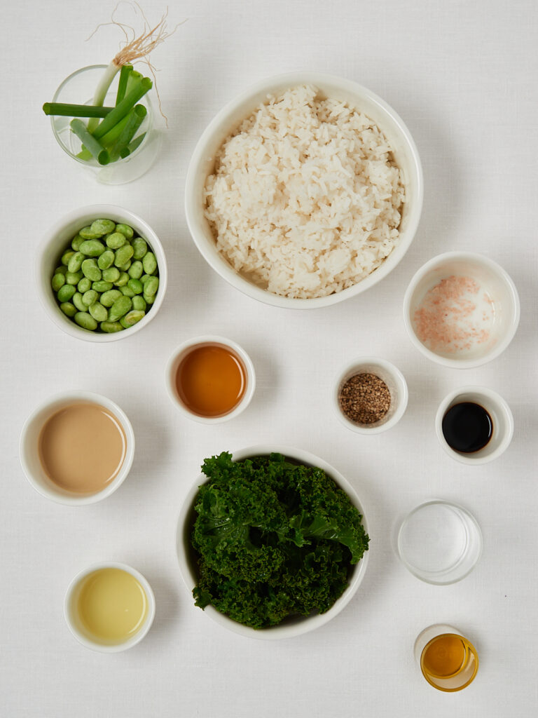 Flatlay of rice, peas, spinach, herbs, spices and dressing ingredients arranged in small bowls.