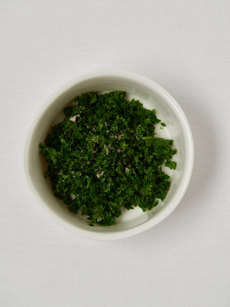 Finely chopped kale massaged with lime juice and salt in a white bowl.