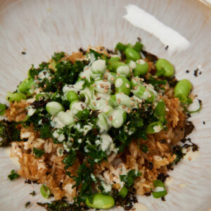 Close-up of a crispy rice bowl with sautéed kale, edamame, sesame seeds and green tahini dressing.