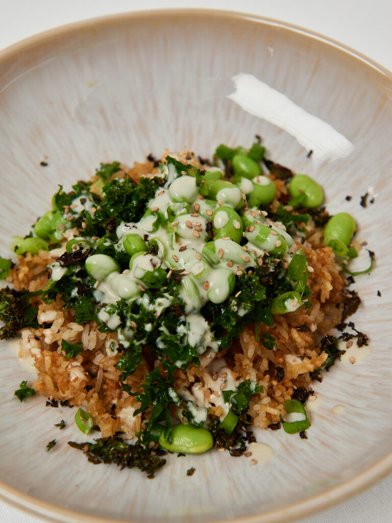 Close-up of a crispy rice bowl with sautéed kale, edamame, sesame seeds and green tahini dressing.