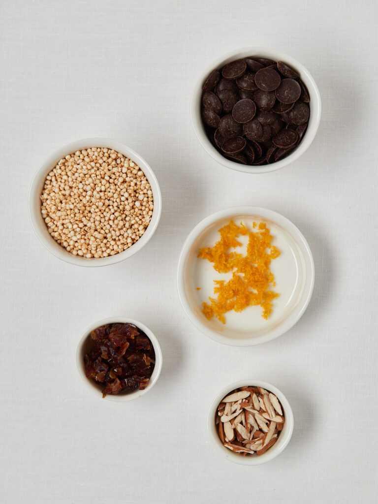 Flatlay of quinoa, seeds, zest and spices in small bowls on a white background