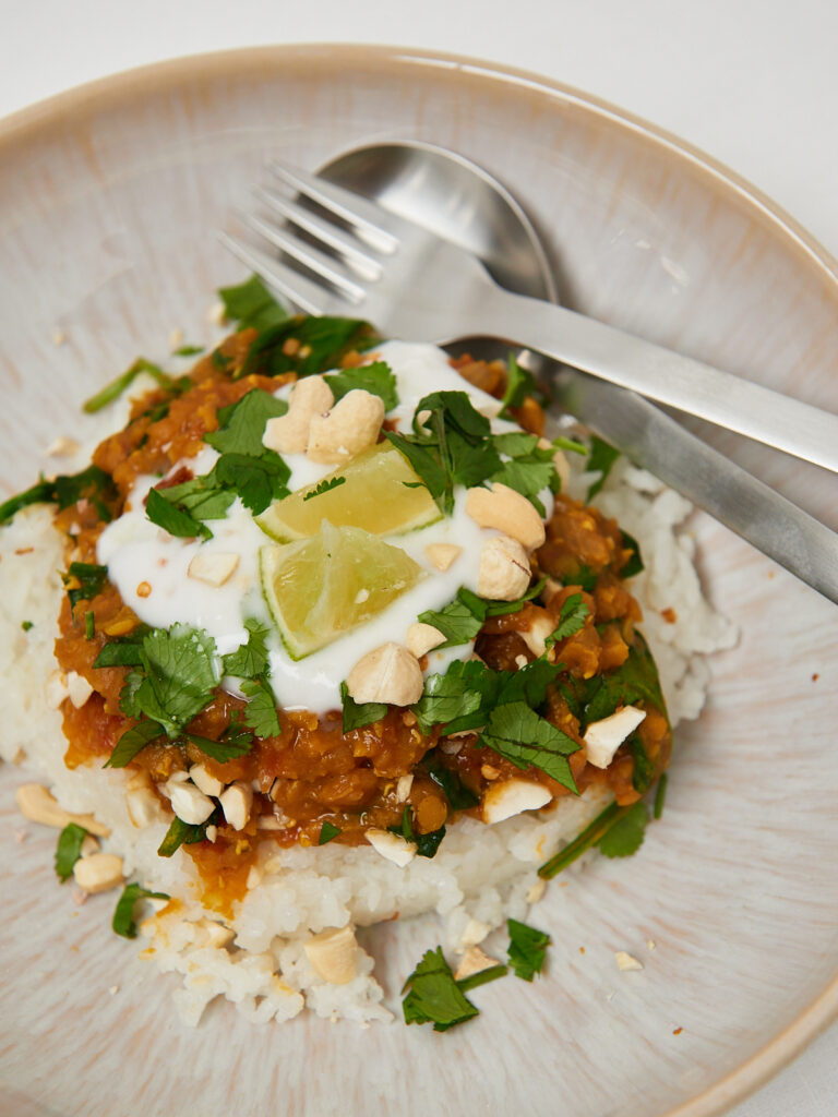 Vegane Linsen-Bowl mit Reis, frischen Kr&auml;utern und Limettenscheiben, serviert auf einem wei&szlig;en Teller mit Gabel.