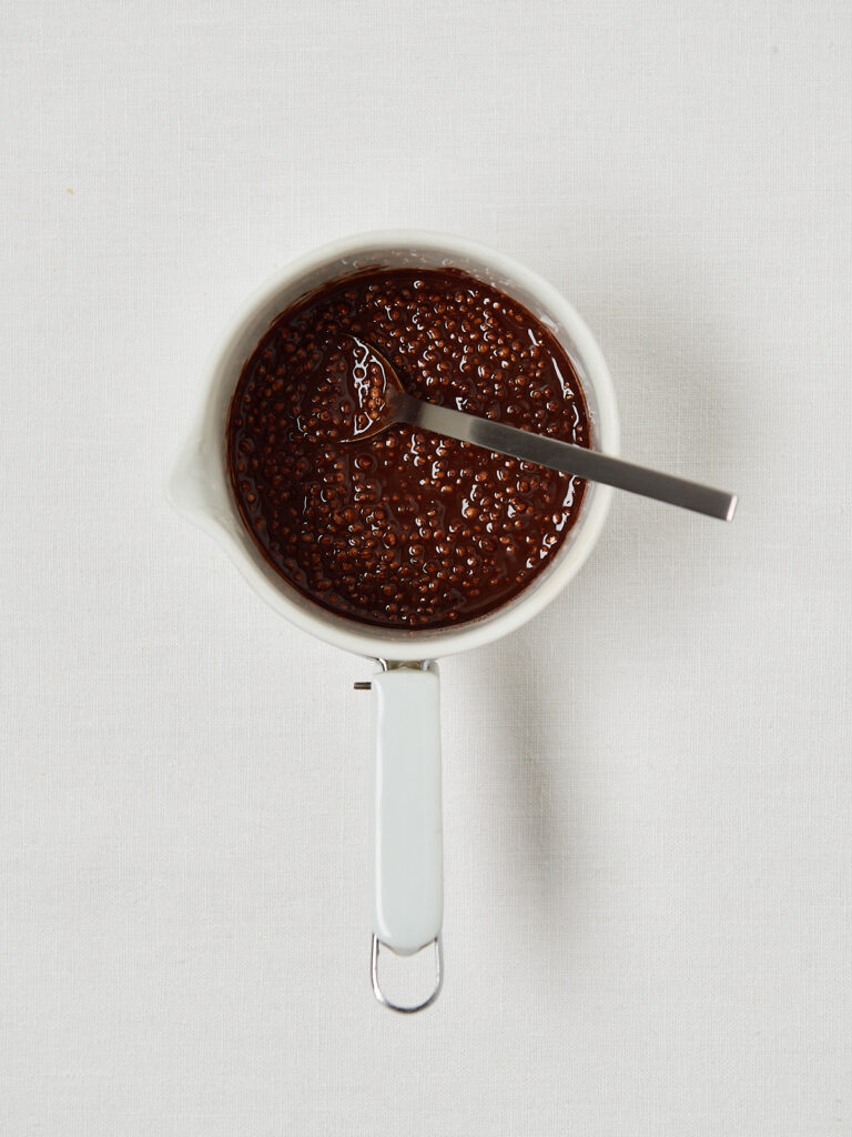 Reihe schokolierter Energy Bites mit knusprigem Topping von oben
Geschmolzene dunkle Schokolade in weißem Messbecher
Flüssige Schokolade mit Kakaopulver und gepufftem Getreide