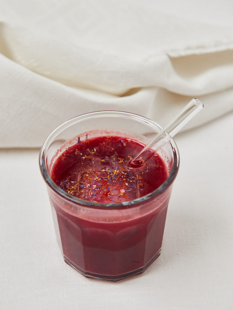 Roter Detox-Saft im Glas mit Glasstrohhalm auf hellem Hintergrund