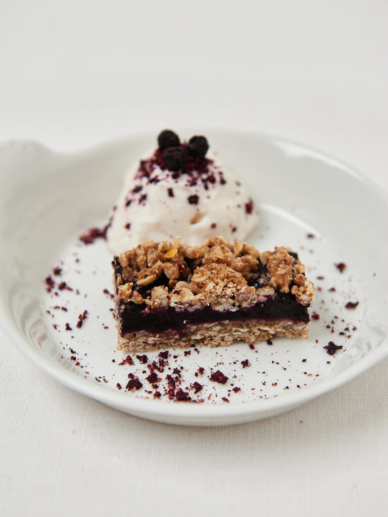 Gesunder Beeren-Crumble-Riegel auf weißem Teller mit Joghurt und Beerenpulver
