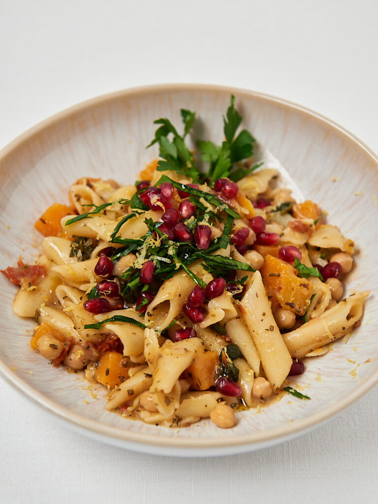 Cremige Pasta mit K&uuml;rbisw&uuml;rfeln, Spinat und Granatapfelkernen, serviert in Keramikschale