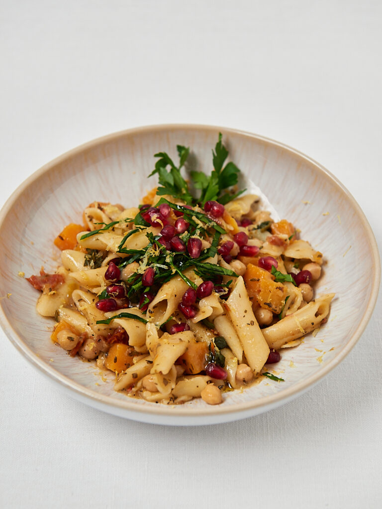One-Pot-Pasta mit cremiger Sauce, Kichererbsen und Granatapfel auf hellem Hintergrund