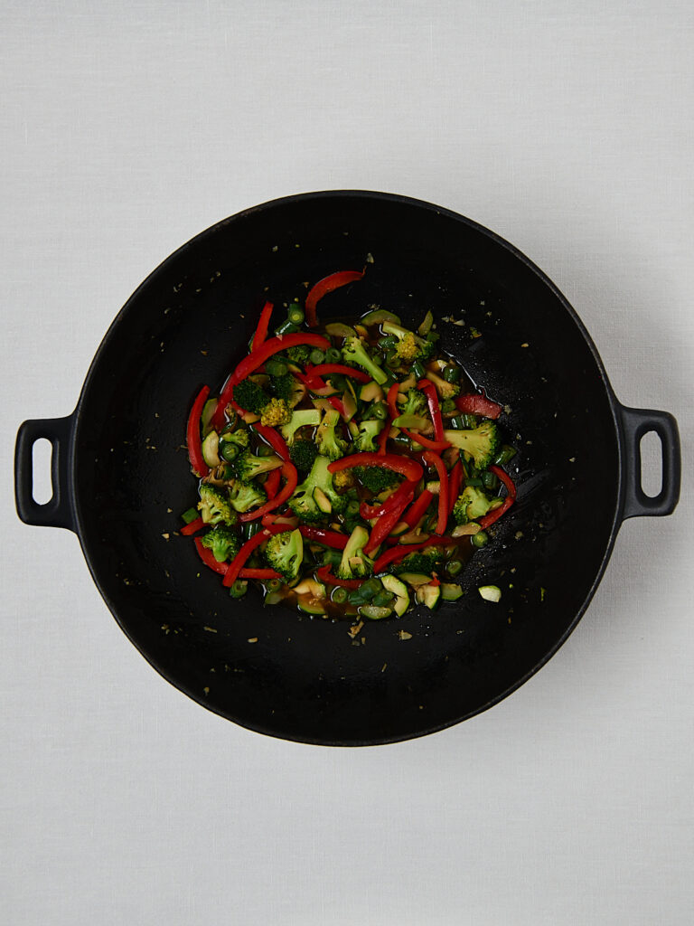 Saut&eacute;ed green vegetables with red bell peppers in pan