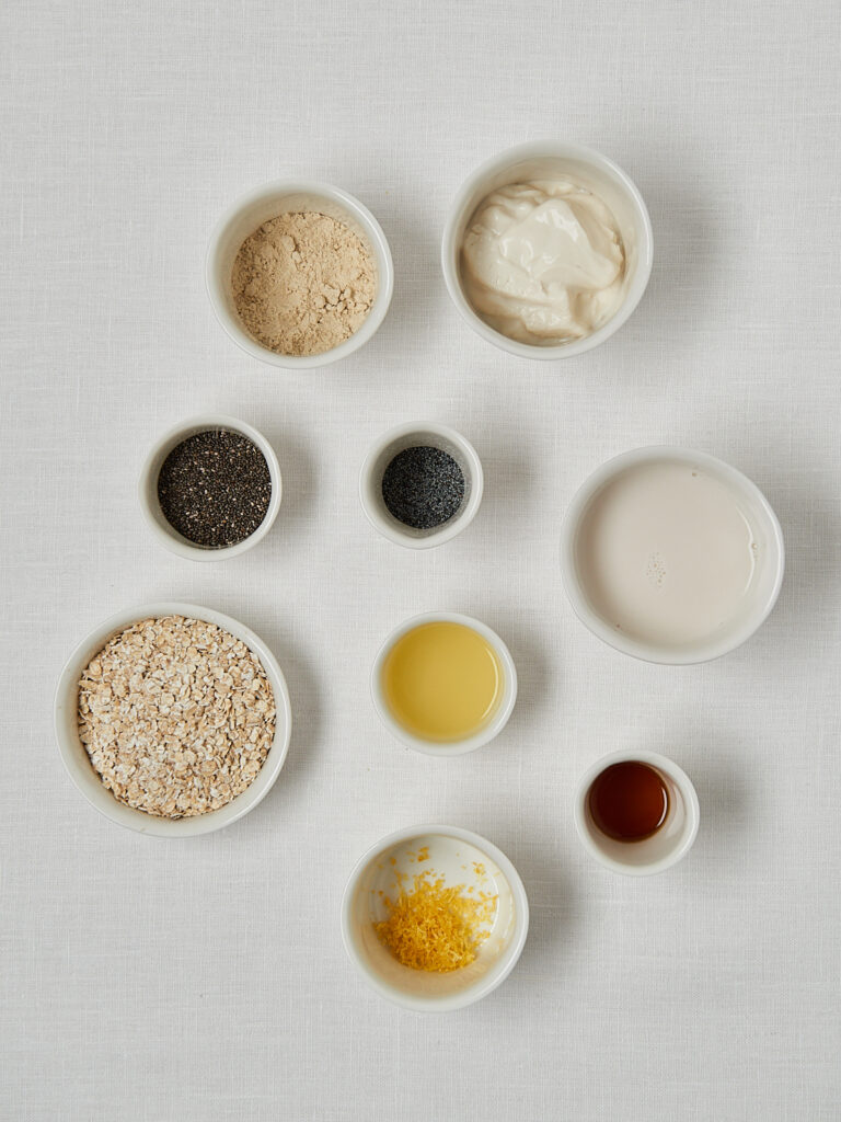 Flatlay Zutaten Zitronen Mohn Overnight Oats: Proteinpulver, Chiasamen, Haferflocken, Ahornsirup und Vanille in kleinen Schälchen