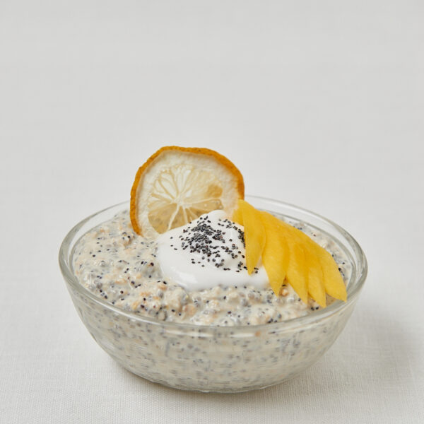 Overnight Oats mit Zitronenscheibe und Joghurt-Topping in Glasschüssel, sommerliches Frühstück