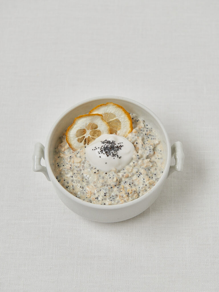 Overnight Oats mit Zitronenscheibe und Mohn in weißer Keramikschüssel, veganes Frühstück