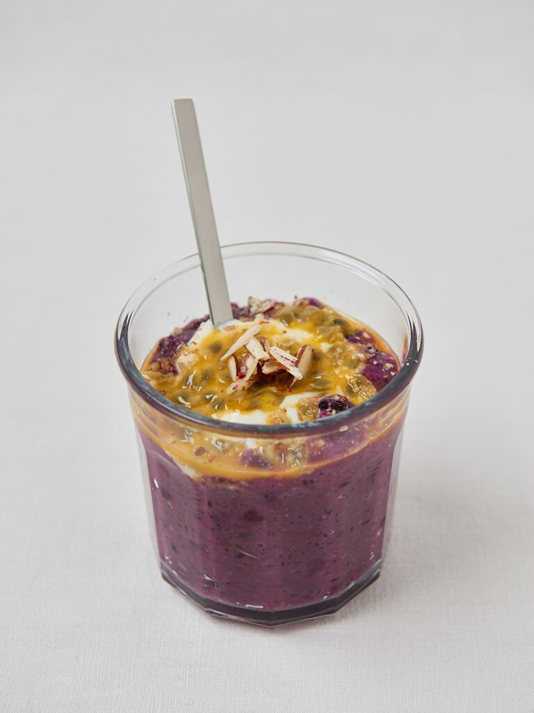 Beeren-Porridge im Glas mit Mandelblättchen und Löffel – seitliche Nahaufnahme